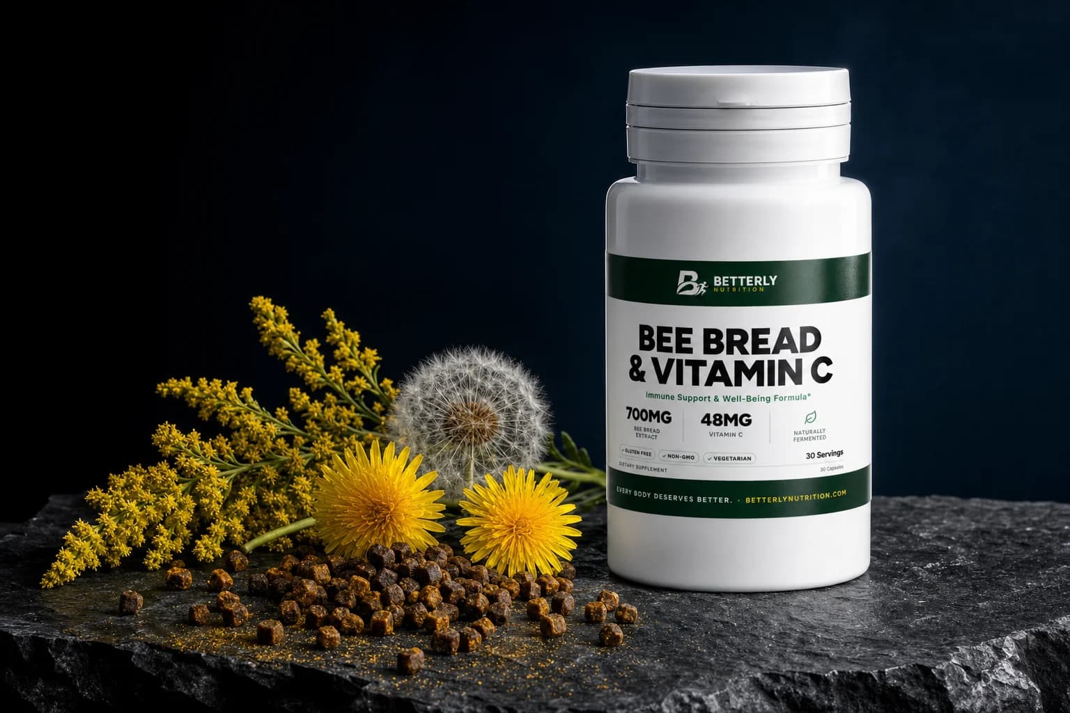 Bee Bread & Vitamin C bottle on dark stone beside a scatter of bee bread granules, two dandelion heads, a seed clock and goldenrod