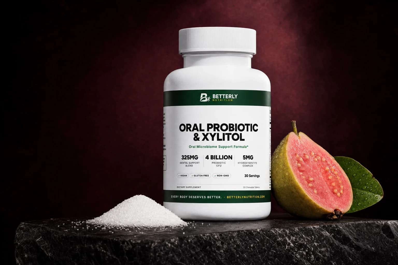 Oral Probiotic & Xylitol bottle on a dark stone slab between a heap of white xylitol crystals and a halved pink guava with a leaf
