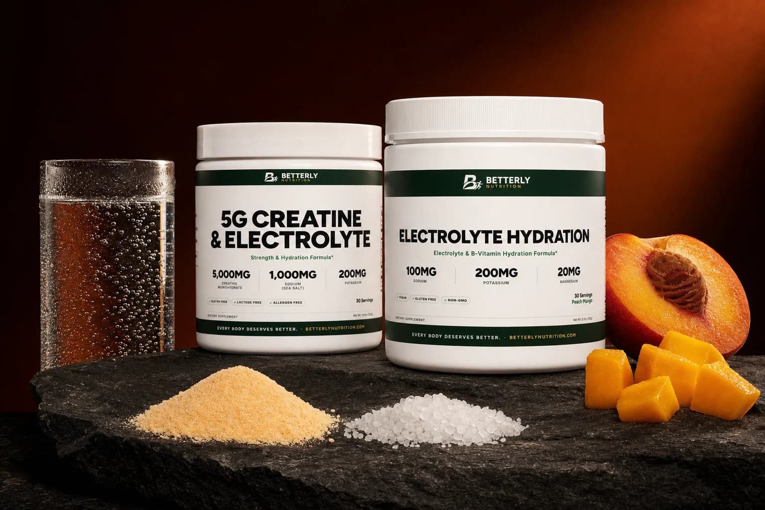 5g Creatine & Electrolyte and Peach Mango Electrolyte Hydration tubs on dark stone with orange powder, sea salt, fizzy water and fruit