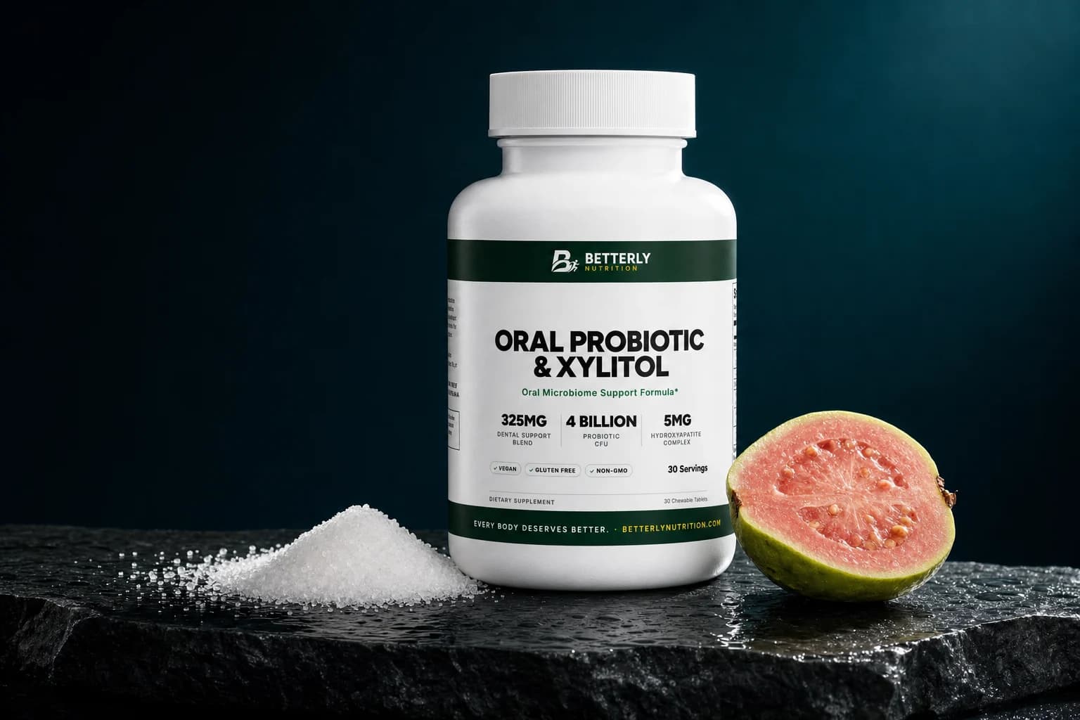 White Oral Probiotic & Xylitol bottle on wet dark slate, a mound of xylitol crystals on its left and a halved pink guava on its right