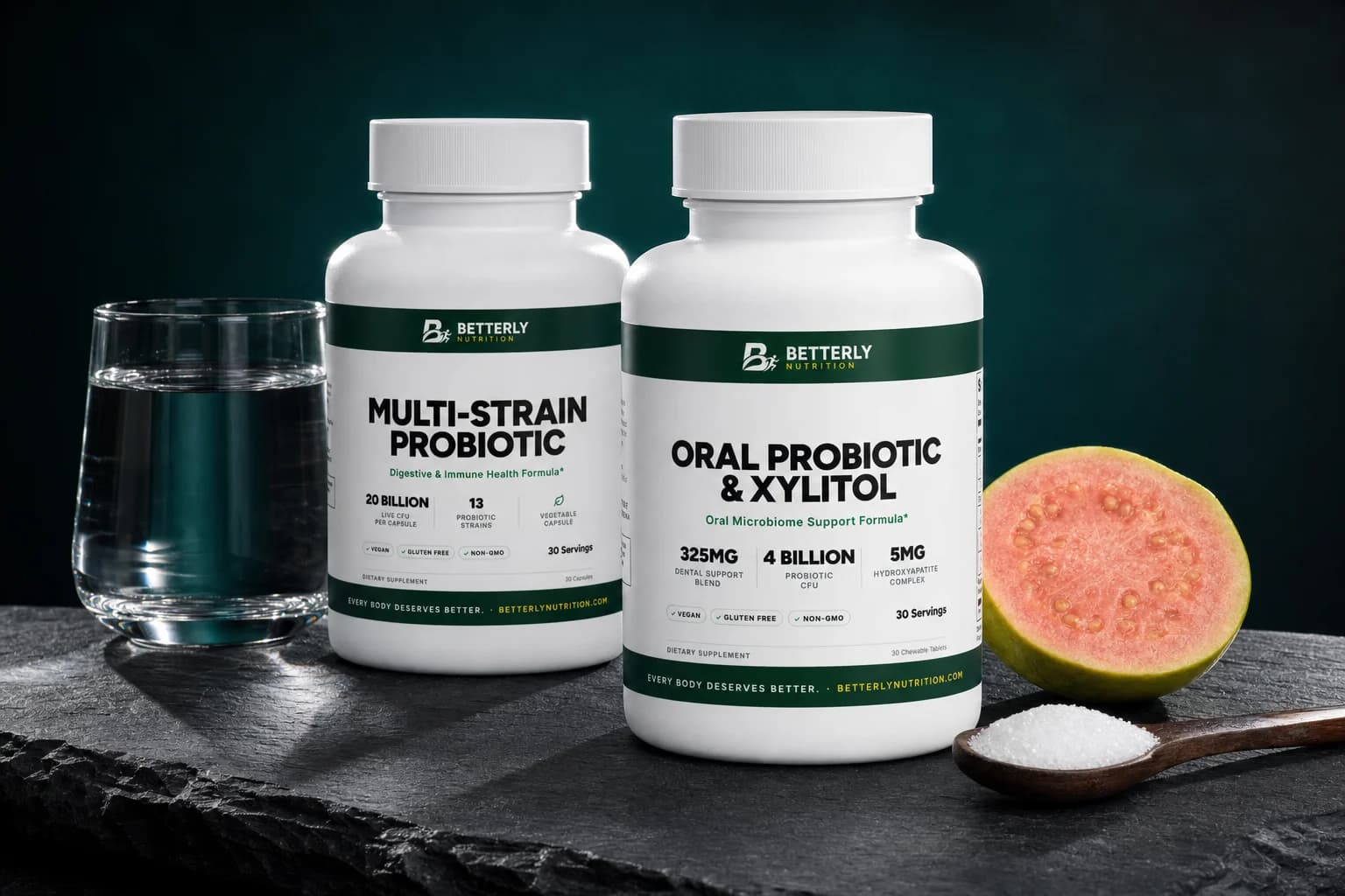 Oral Probiotic & Xylitol and Multi-Strain Probiotic bottles on dark slate with a halved guava, a spoon of xylitol and a glass of water