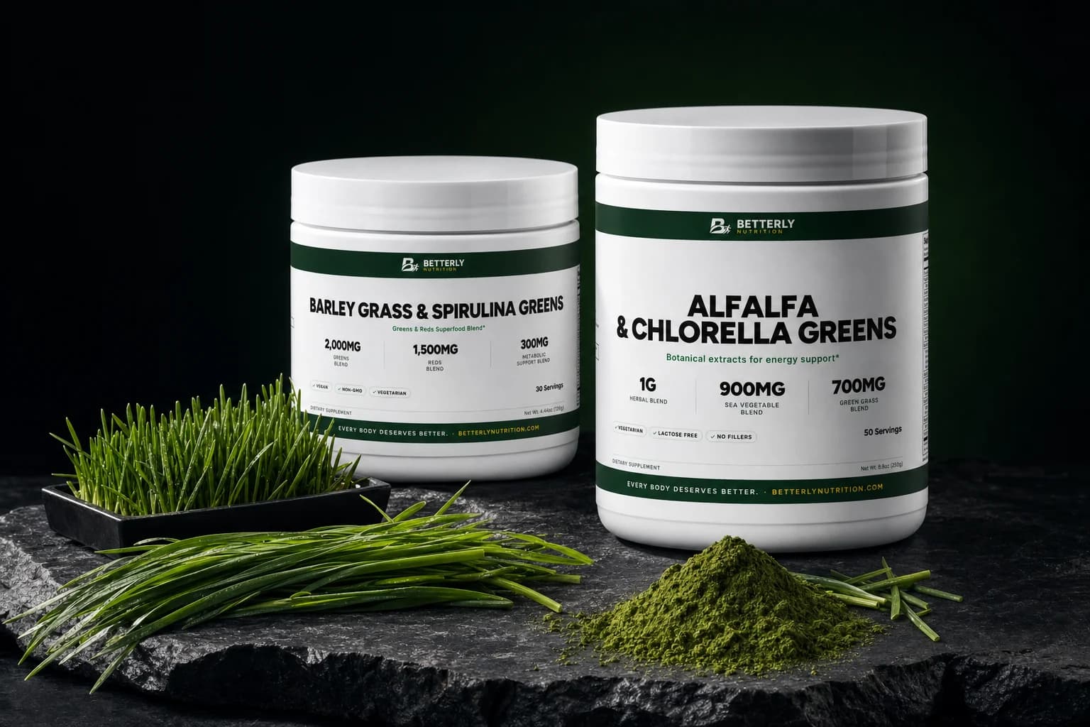 Barley Grass & Spirulina and Alfalfa & Chlorella Greens tubs on dark slate beside a tray of wheatgrass, cut grass blades and green powder